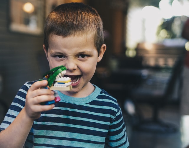 bambino che gioca con la testa di un dinosauro giocattolo, uno dei tanti regali di compleanno per bambini